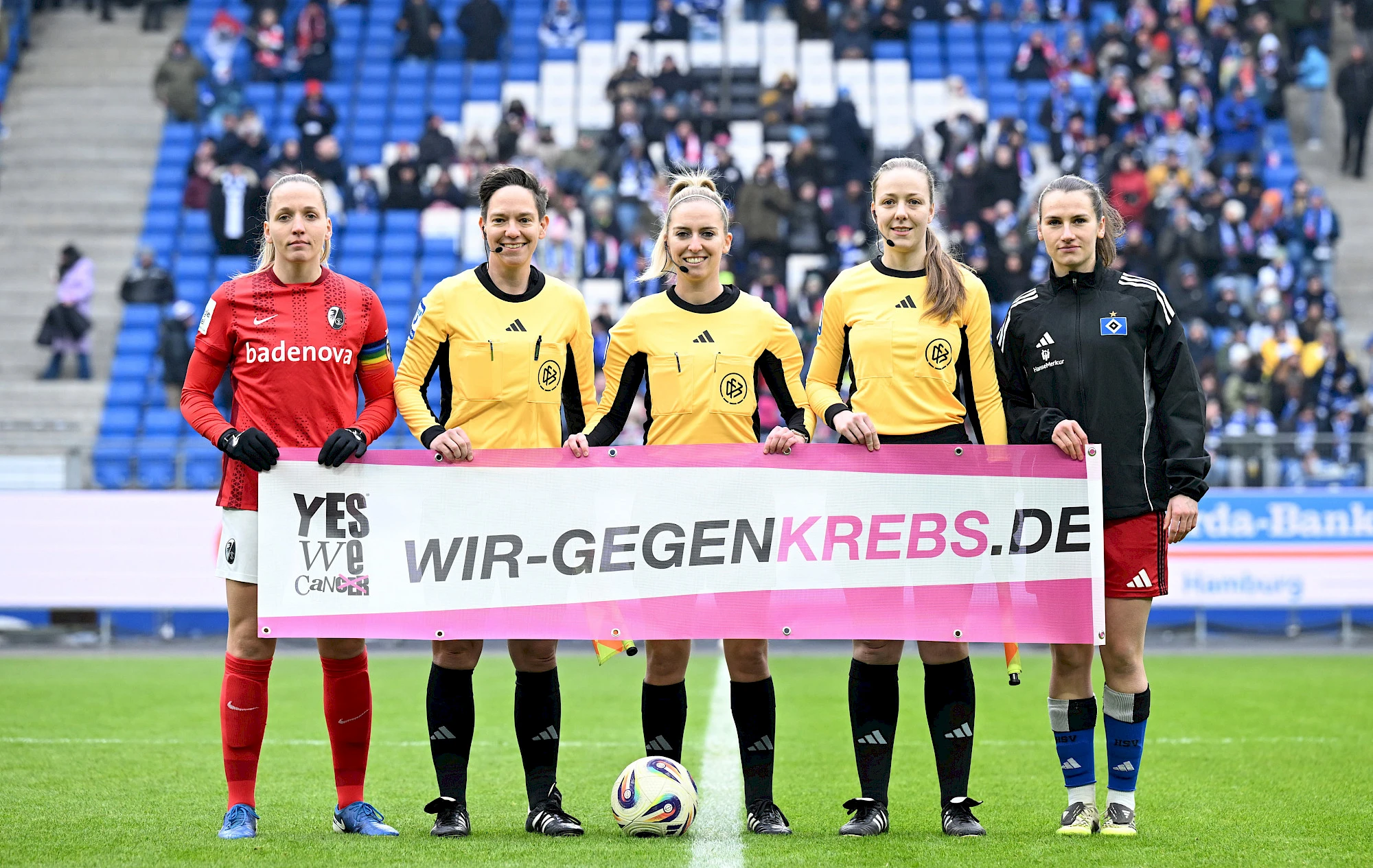 Starke Botschaft vor dem Spiel: Die beiden Kapitäninnen und das Schiedsrichterinnen-Gespann mit dem Aktionsbanner zu "Wir gegen Krebs"